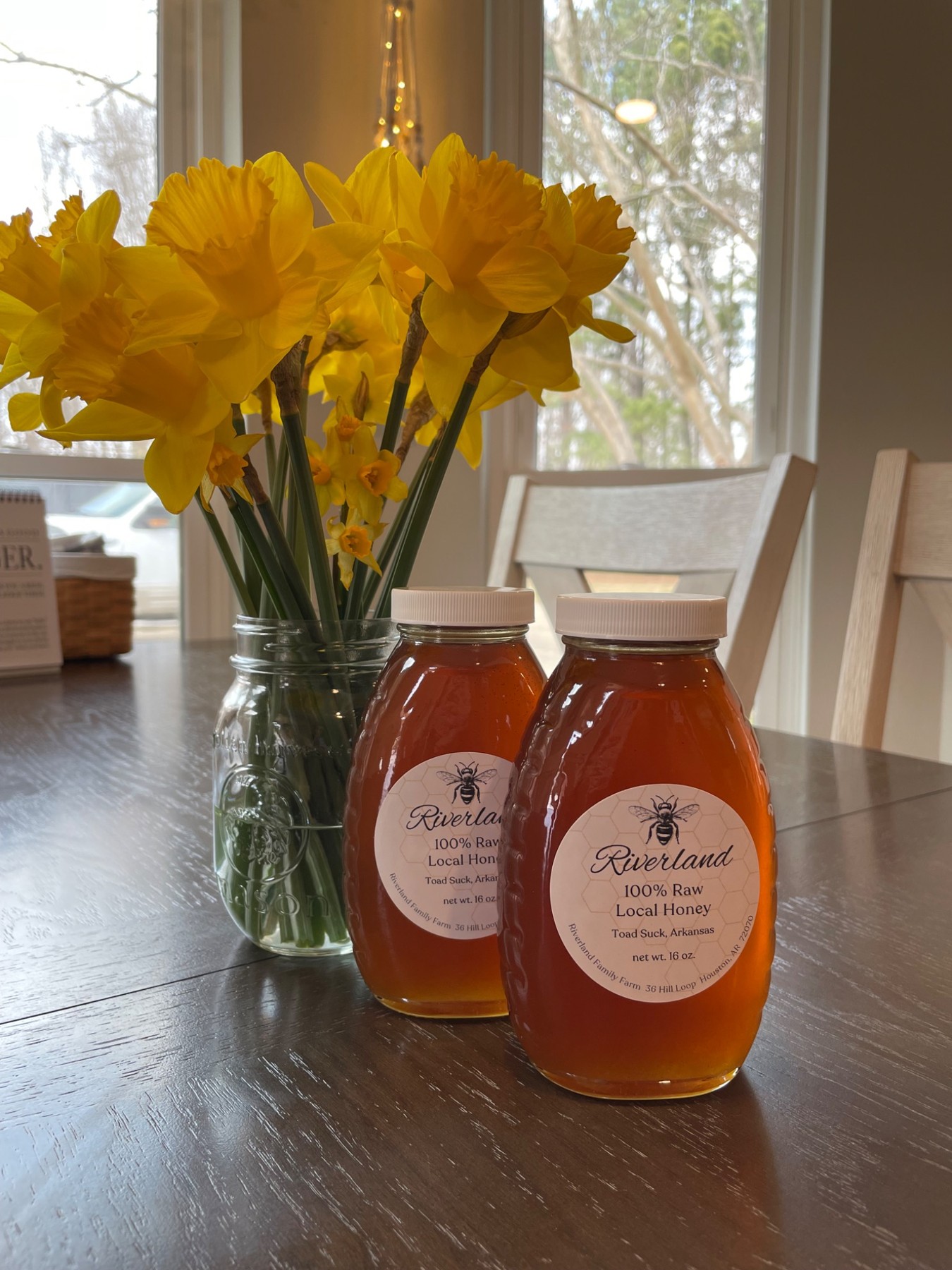 Two jars of Riverland honey beside a vase of yellow daffodils